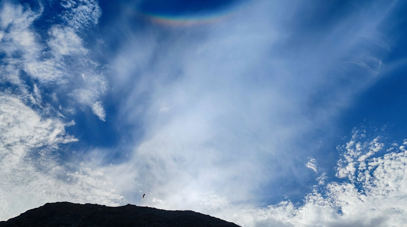 Gleitschirme fliegen über einem Bergrücken unter blauem Himmel mit Wolken und Halo-Effekt